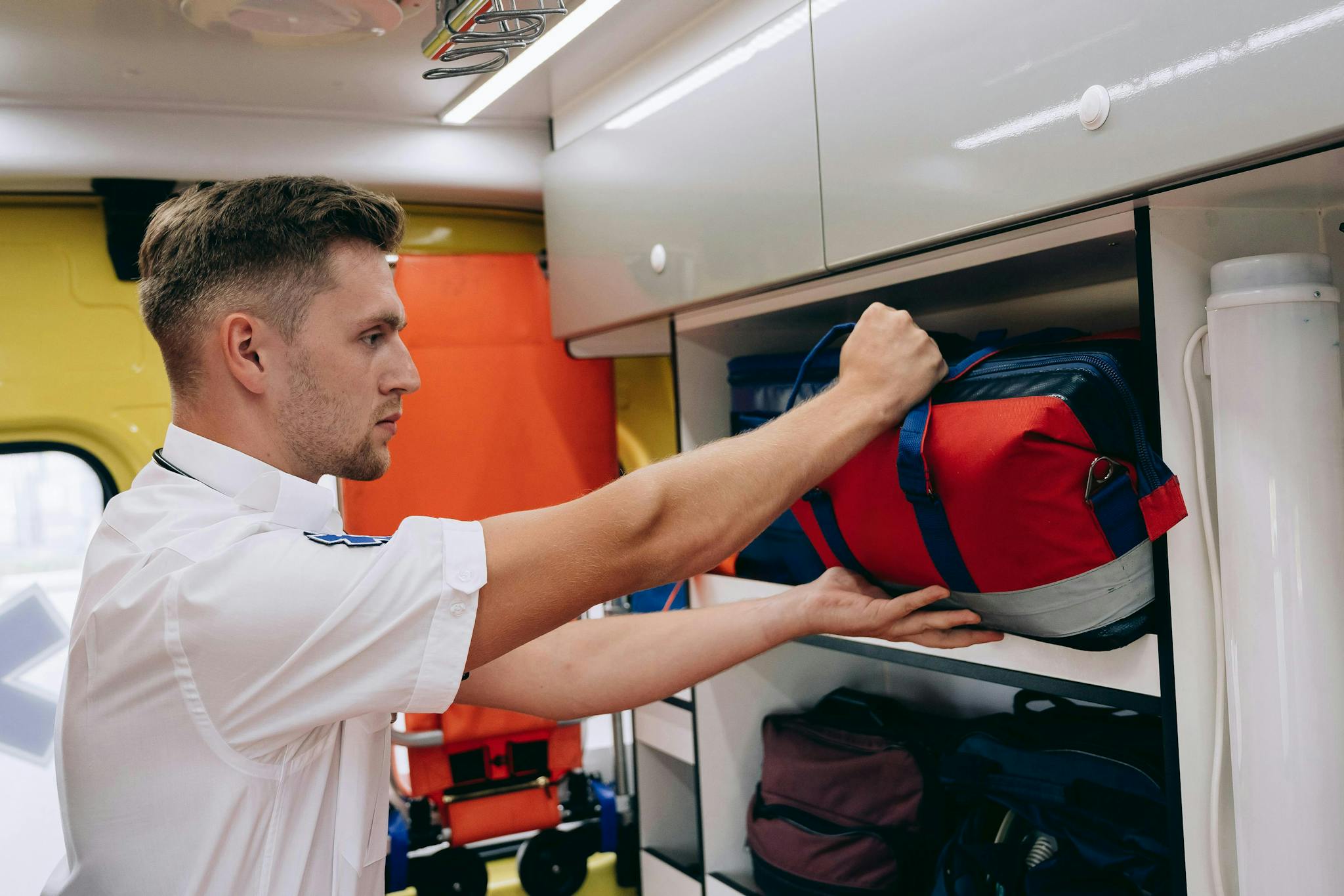 A paramedic places a medical bag on a shelf inside an ambulance, preparing for emergencies.