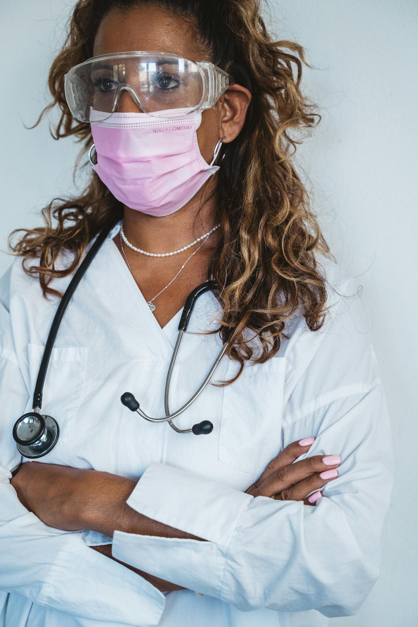 Portrait of a female doctor with a stethoscope, face mask, and protective goggles.